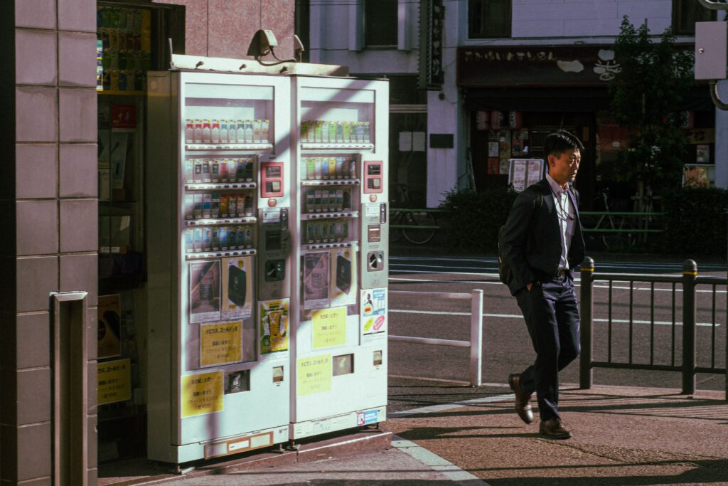 Businessman passing vending machines on a Tokyo street during daytime.
